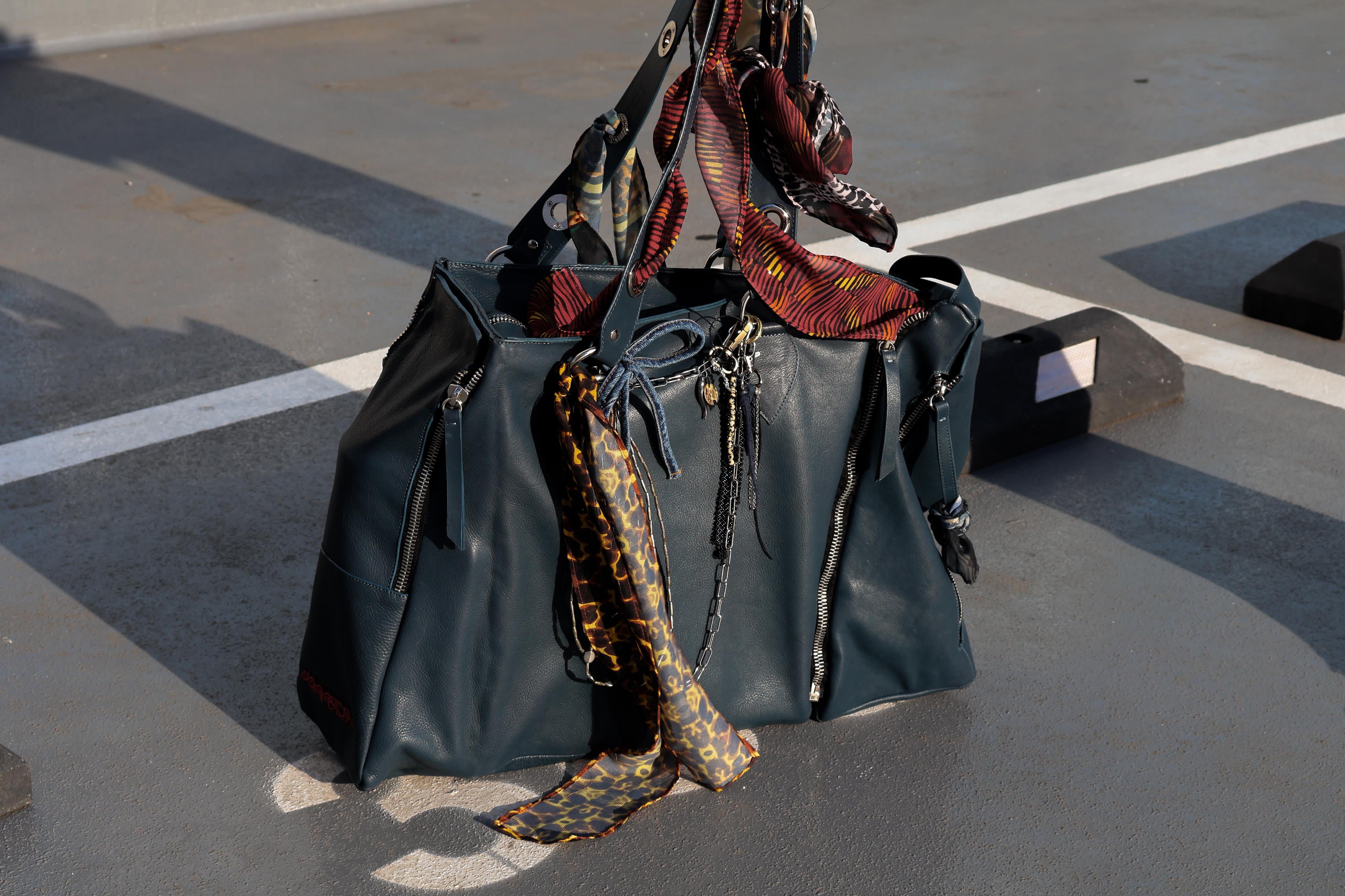 Bolso de piel verde azulado del sistema NOMMADA, con pañuelos estampados y accesorios colgando de las asas, fotografiado en exteriores urbanos.
